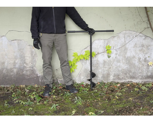 Person mit Erdlochbohrer im Garten