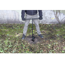 Eine Person verwendet einen Erdbohrer, um ein Loch in den Boden zu bohren.