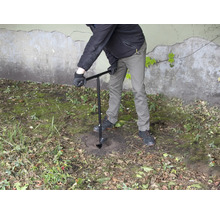 Eine Person bohrt mit einem Erdbohrer ein Loch in den Boden.