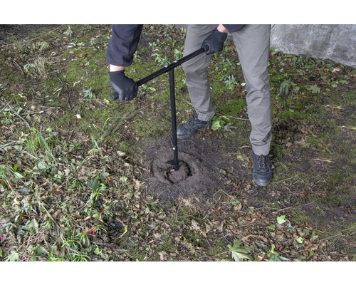 Eine Person benutzt einen Erdbohrer, um ein Loch in den Boden zu bohren.