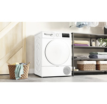 Freistehender weißer Bosch Wärmepumpentrockner in einem hellen Raum mit Wäschekorb und Regal