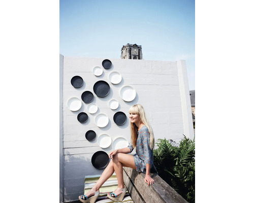 Dekorative Teller in unterschiedlichen Größen an einer Wand im Außenbereich mit einer Frau, die auf einer Bank sitzt