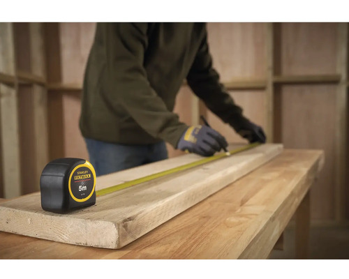 Handwerker misst ein Holzbrett mit einem Stanley Fatmax Rollbandmass, Länge 5 Meter.