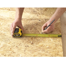 Eine Person misst ein Stück Holz mit einem Stanley Fatmax Rollbandmass von 5 Metern und markiert es mit einem Stift.