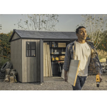 Gartenschuppen mit offenstehender Tür und einer Person, die Werkzeuge und Holz trägt