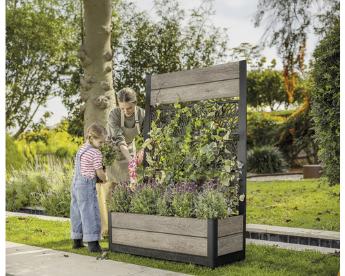 Frau und Kind bepflanzen einen Pflanzkasten mit Rankgitter im Garten.