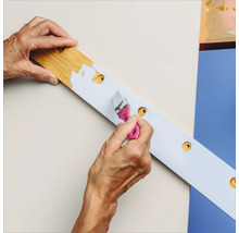 Eine Person streicht ein Holzbrett mit einer Reihe von Löchern mit einem Pinsel.