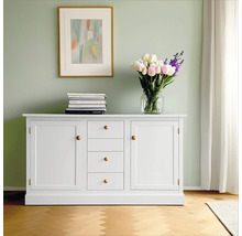 Weißes Sideboard mit Schubladen und Schranktüren, Bücherstapel, Blumenstrauß und gerahmtem Bild