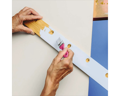 Eine Person streicht eine Holzleiste mit einer Lackierbürste.