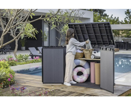 Aufnahme einer Frau, die eine Aufbewahrungsbox im Außenbereich auf einer Holzterrasse neben einem Pool benutzt, um Gegenstände zu verstauen