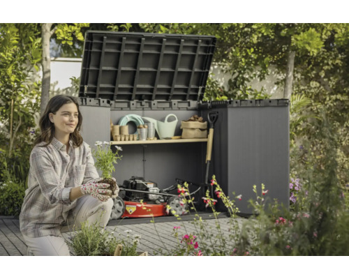 Frau vor einer geöffneten Gerätebox mit Gartengeräten und Rasenmäher