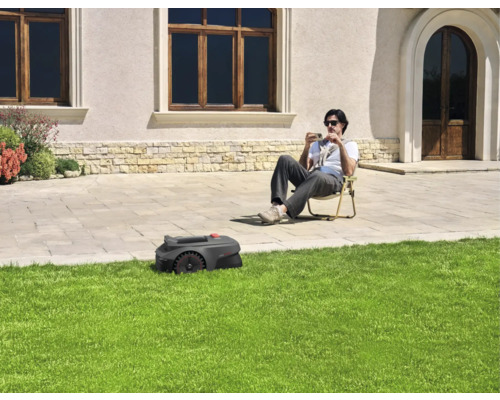 Ein Rasenmähroboter mäht den Rasen, während eine Person im Garten sitzt.