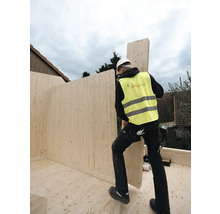 Ein Bauarbeiter mit Schutzweste und Helm montiert eine Holzwand auf einer Baustelle.