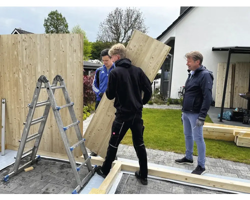 Aufbau einer Holzgartenmauer mit Helfern und Leiter.
