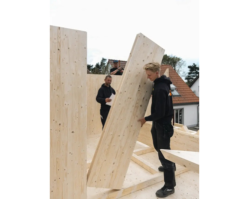 Drei Handwerker montieren eine Holzkonstruktion für ein Gebäude.