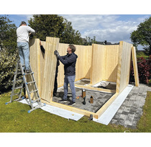 Aufbau eines Holzgartenhauses mit drei Personen auf einer Rasenfläche