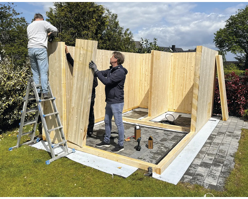 Aufbau eines Holzgartenhauses mit drei Personen auf einer Rasenfläche