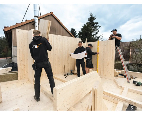 Bauarbeiter errichten ein Holzhaus mit Holzplatten nach Bauplan.