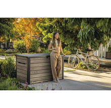 Szene im Garten mit einer Frau, die sich an eine Aufbewahrungsbox aus Holz lehnt und einen Kaffeebecher hält.