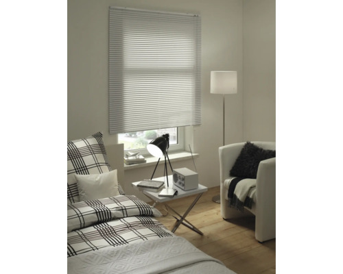 Wohnraum mit Bett, Sessel, Stehlampe, Tisch und Fenster mit Jalousie