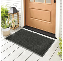 Graue Fußmatte vor einer Haustür auf einer Veranda mit Pflanzen und Windlicht