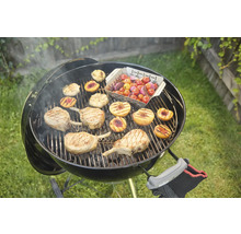 Kugelgrill mit Grillgut wie Fleisch, Pfirsichen und Tomaten auf dem Rost