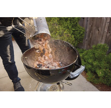 Person schüttet Grillkohle aus einem Anzündkamin in einen Kugelgrill.