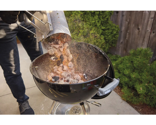 Person schüttet Grillkohle aus einem Anzündkamin in einen Kugelgrill.