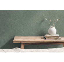 Grüne Vliestapete mit Strukturmuster im Raum mit Holzbank, Büchern und Blumenvase
