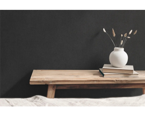 Dekorative Szene mit Holzbank, Büchern und Vase mit getrockneten Blumen vor dunkler Wand