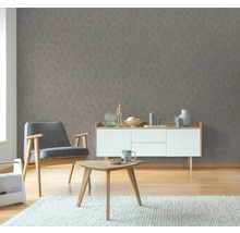 Wohnzimmer mit grauer Mustertapete, Sessel, Beistelltisch und Kommode.
