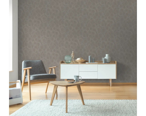 Wohnzimmer mit grauer Mustertapete, Sessel, Beistelltisch und Kommode.