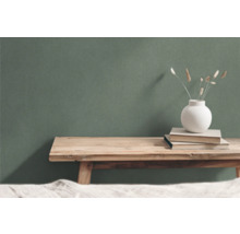 Dekorative Szene mit Holztisch, Büchern und Vase vor grüner Wand