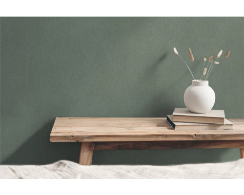 Dekorative Szene mit Holztisch, Büchern und Vase vor grüner Wand