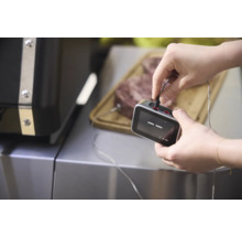 Ein Mann schließt ein Grillthermometer an ein Stück Fleisch an, das auf einem Schneidebrett liegt.