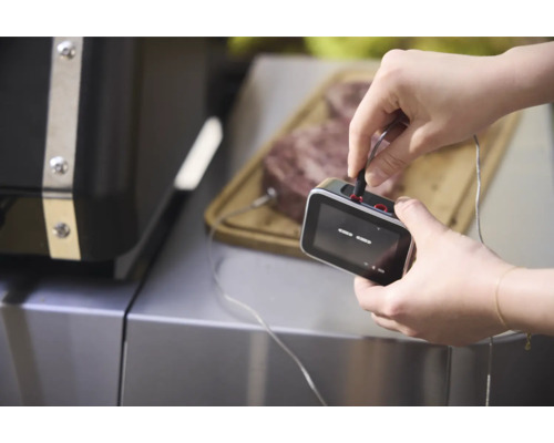 Ein Mann schließt ein Grillthermometer an ein Stück Fleisch an, das auf einem Schneidebrett liegt.