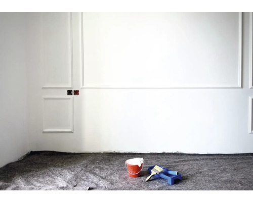 Renovierungsarbeiten mit Farbeimer, Pinsel und Farbroller vor weißer Wand mit Stuckelementen