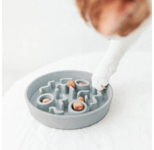 Grauer Fressnapf mit Labyrinthstruktur und Hundefutter, eine Hundepfote ist zu sehen.