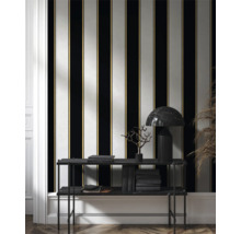 Raumansicht mit gestreifter Tapete in Schwarz, Weiß und Gold, sowie Regal mit Büchern und Lampe.