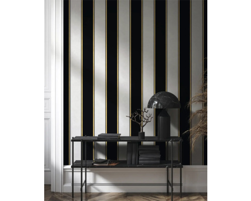 Raumansicht mit gestreifter Tapete in Schwarz, Weiß und Gold, sowie Regal mit Büchern und Lampe.