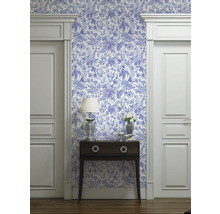Raumansicht mit blau-weiß gemusterter Tapete, Kommode, Lampe und Türrahmen