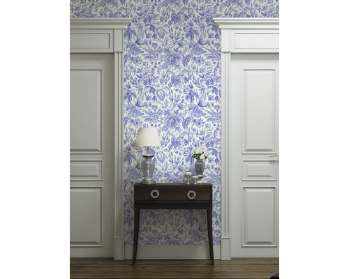 Raumansicht mit blau-weiß gemusterter Tapete, Kommode, Lampe und Türrahmen
