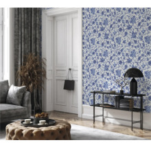 Wohnzimmer mit blumiger Tapete, Couch, Hocker und Dekorationen für ein gemütliches Ambiente