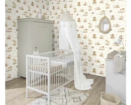 Kinderzimmer mit Gitterbett, Wickelkommode und Schrank vor einer Tapete mit Tiermotiven.