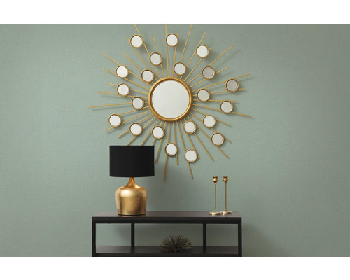 Dekoratives Interieur mit Spiegel in Sonnenform, Lampe und Kerzenständern auf einem Regal.