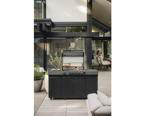 Außenszene mit einem schwarzen Gasgrill mit geöffnetem Deckel, unter dem Grillgut liegt.