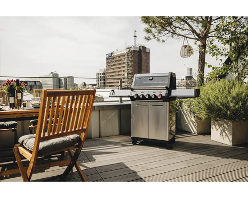 Edelstahl Grill auf einer Dachterrasse neben einem Holztisch und Stühlen.
