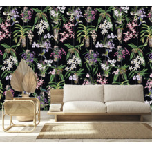 Raumansicht mit einer Tapete mit Orchideen- und Kolibrimuster hinter einem Sofa, einem Sessel und einer getrockneten Palme.
