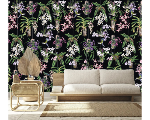 Raumansicht mit einer Tapete mit Orchideen- und Kolibrimuster hinter einem Sofa, einem Sessel und einer getrockneten Palme.