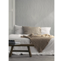 Schlafzimmer mit Bett, Tagesdecke, Kissen, Bücherstapel und Tapete mit Wellenmuster